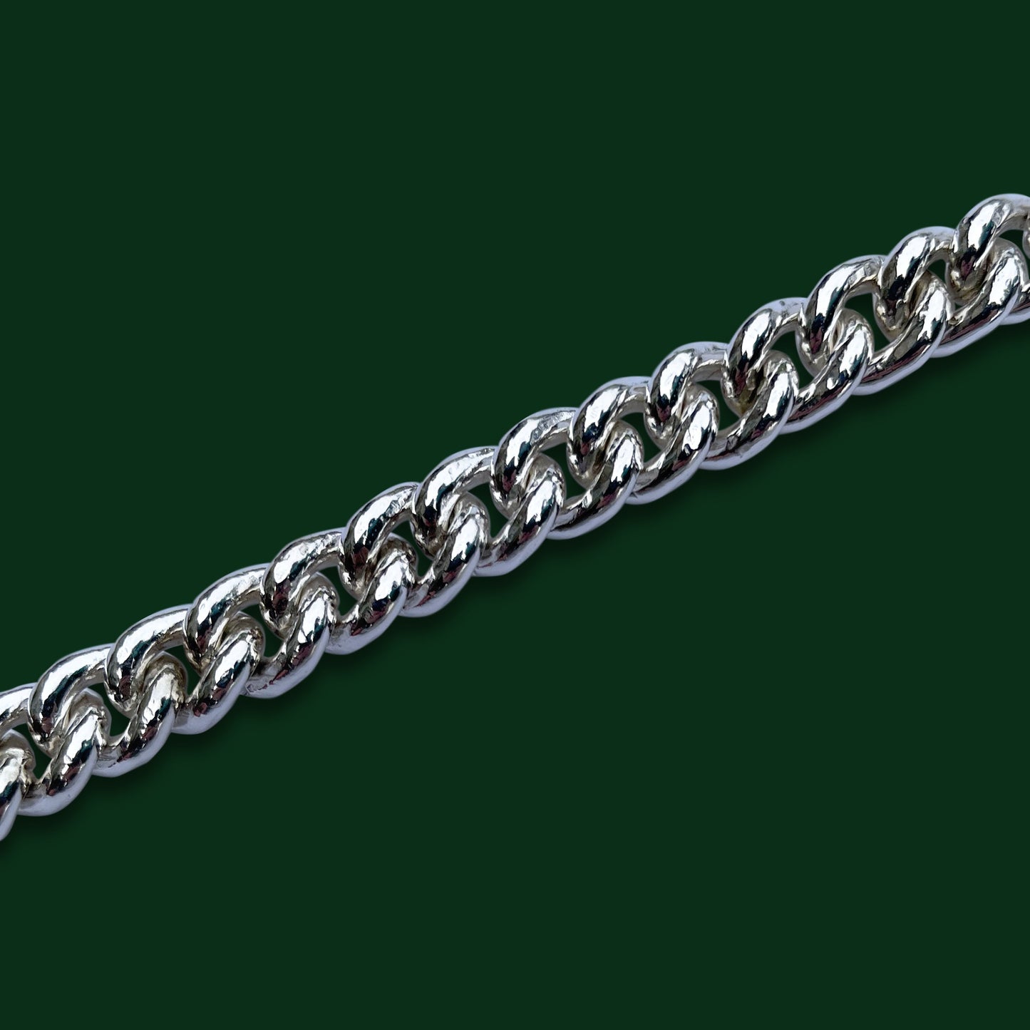 A close up of Timio's Curb chain, in medium weight, on a dark green background.