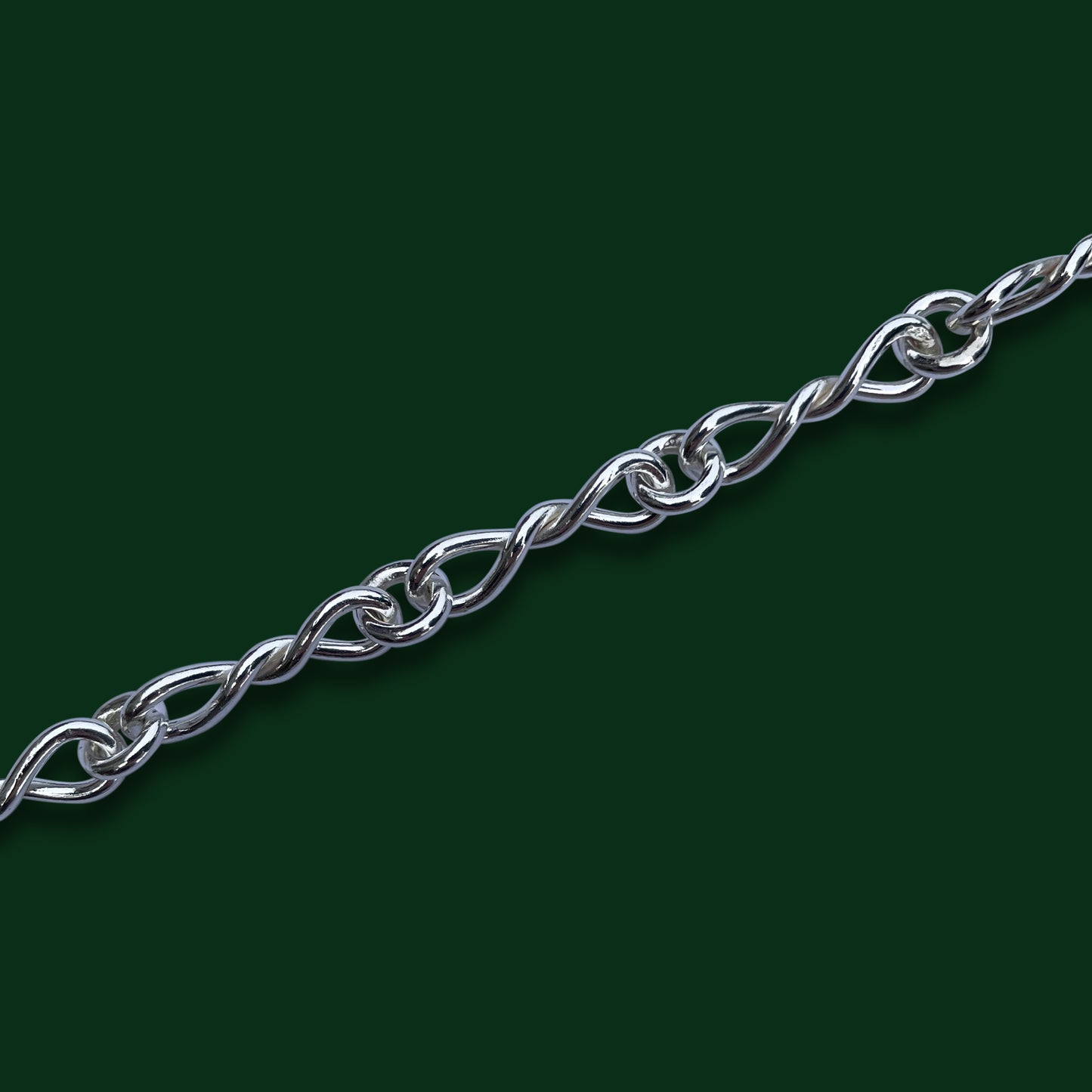 A close up of Timio's Bolero chain, emphasizing the small bow-shaped links, on a dark green background.