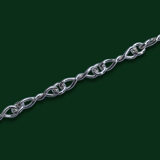 A close up of Timio's Bolero chain, emphasizing the small bow-shaped links, on a dark green background.