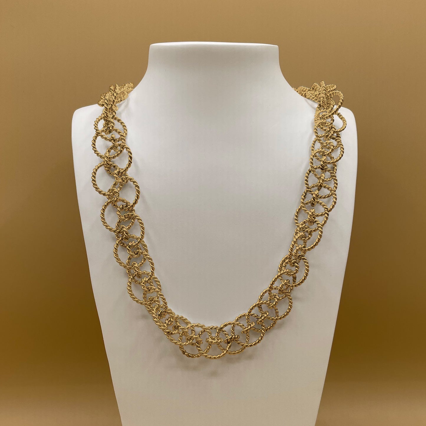Timio's Ethereal chain in 24 karat gold, displayed on a white bust in front of a golden background.