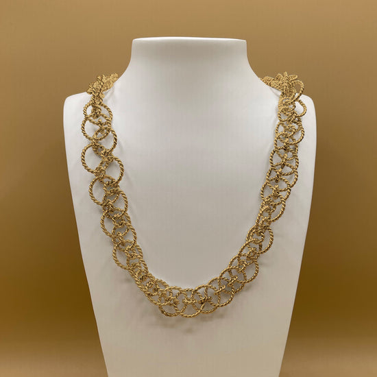 Timio's Ethereal chain in 24 karat gold, displayed on a white bust in front of a golden background.