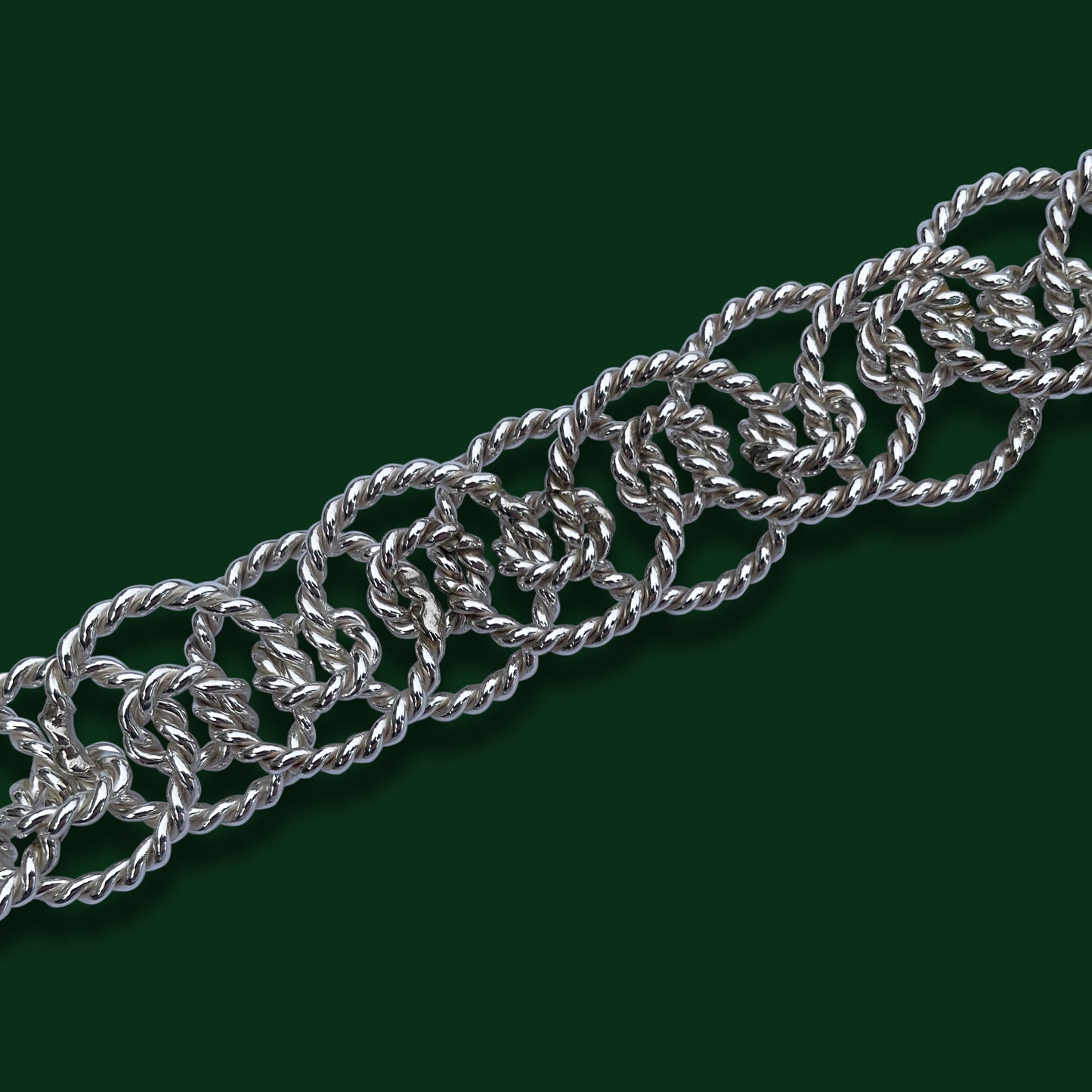 A close up of Timio's Ethereal chain on a dark green background to emphasize the twisted circle links of various sizes.