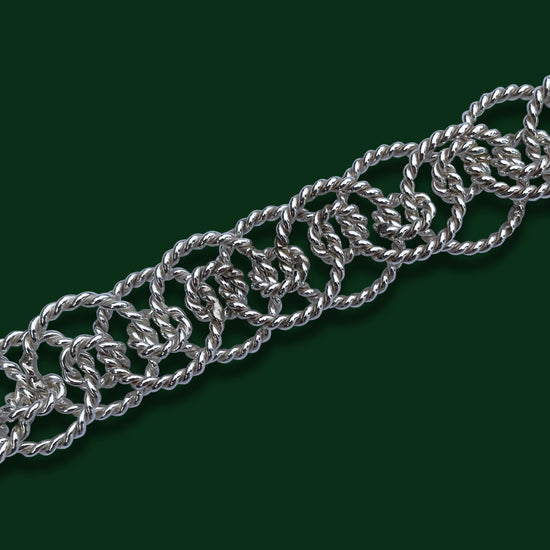 A close up of Timio's Ethereal chain on a dark green background to emphasize the twisted circle links of various sizes.