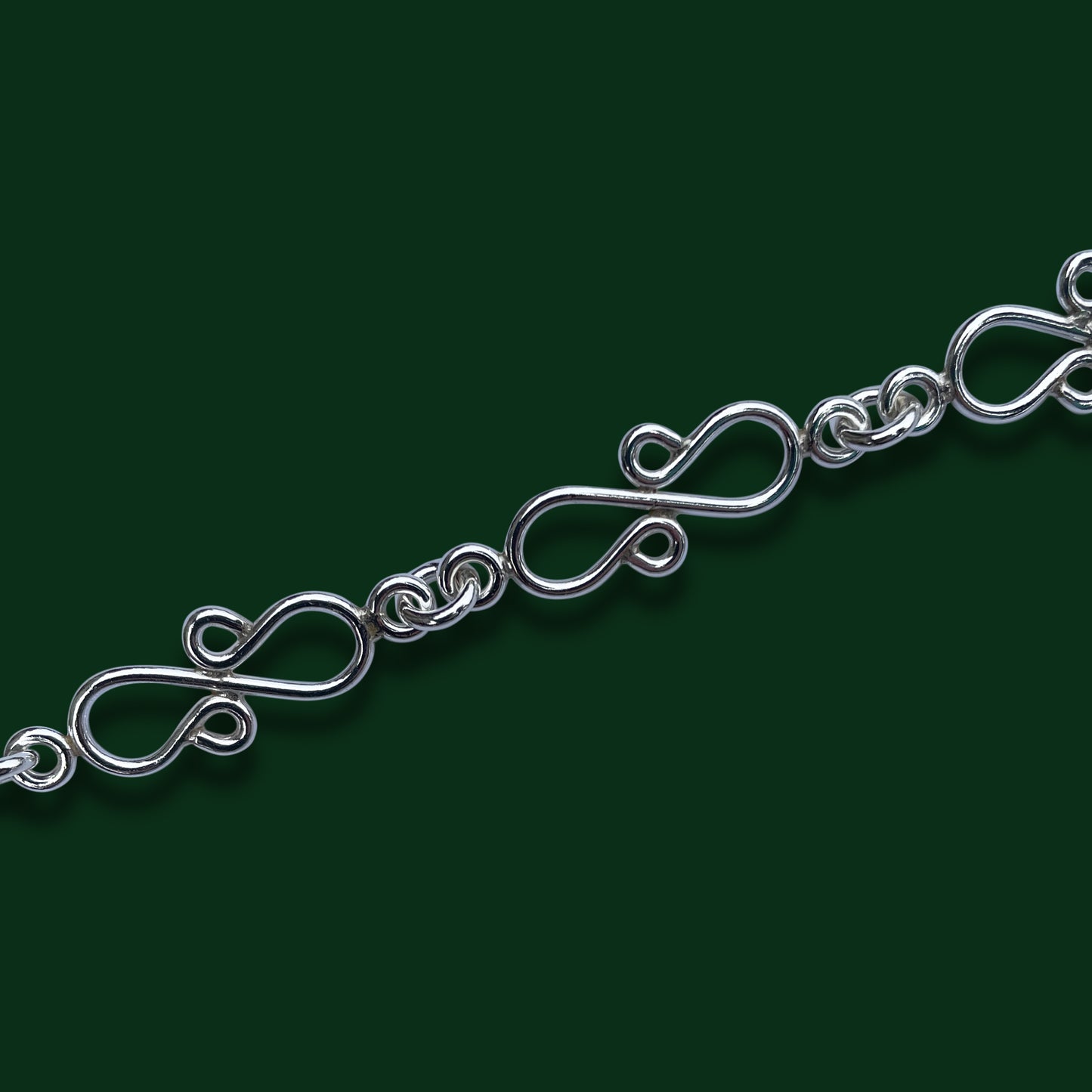 A close up of Timio's Jubilee chain, emphasizing its figure-eight inspired links on a dark green background.