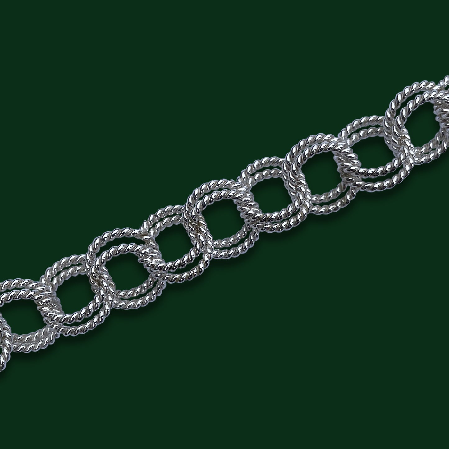 A close up of Timio's Laurel chain on a dark green background to emphasize the pairs of twisted circles linked together.
